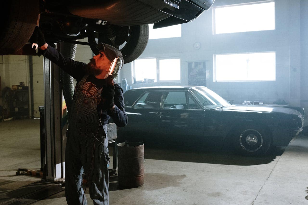 Mastering the First Impression: Your intriguing post title goes here Mechanic working under a lifted car in an indoor garage setting with vintage vehicle in background.